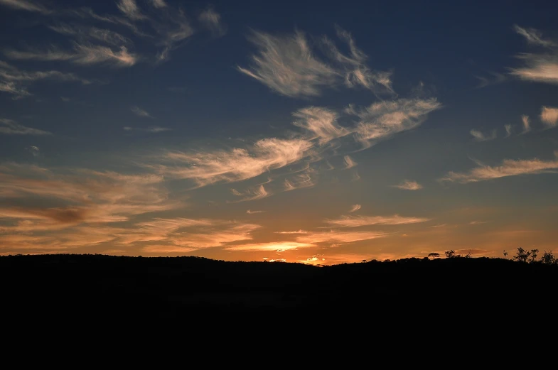 the sun rises behind a hill as clouds float across