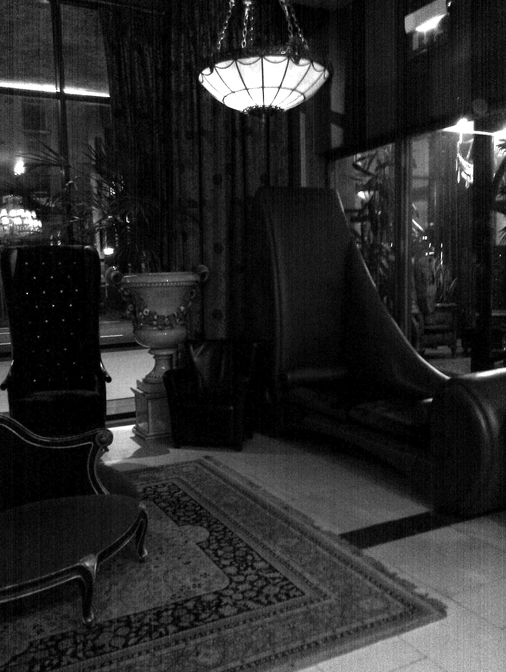 black and white po of large chair, piano, table, and rug in an old looking room