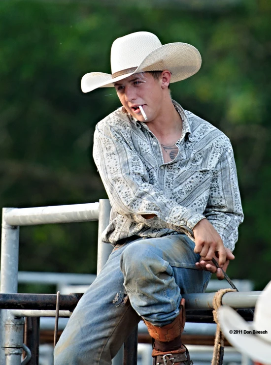 a boy in jeans and a cowboy hat smoking a cigarette