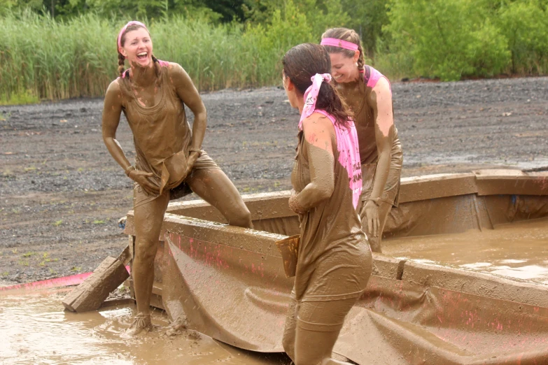 three girls in mud suits playing in a small boat