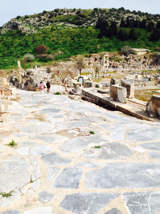 a stone pathway leads to ancient buildings and people walking