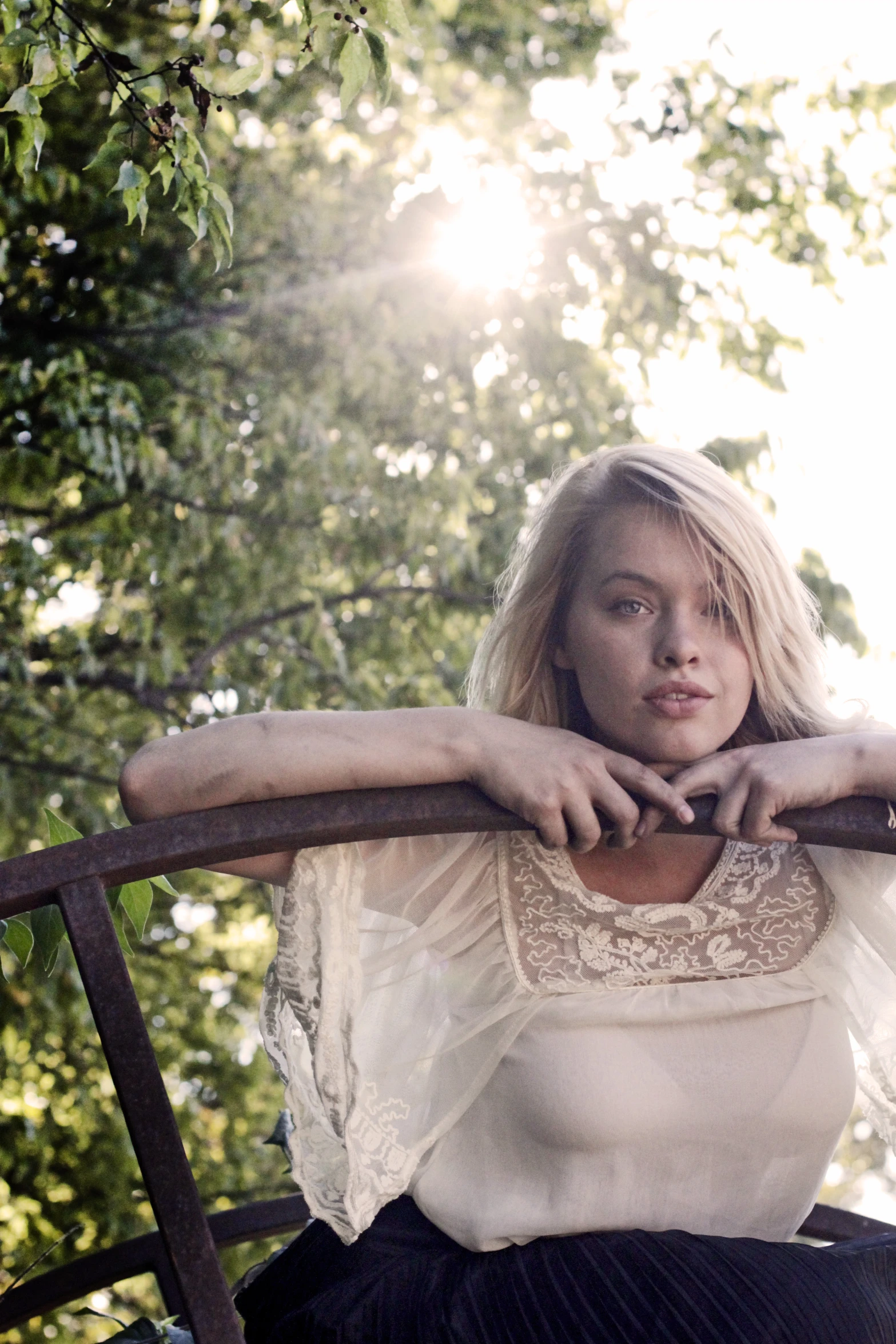 the blonde woman is sitting on the porch leaning against the fence