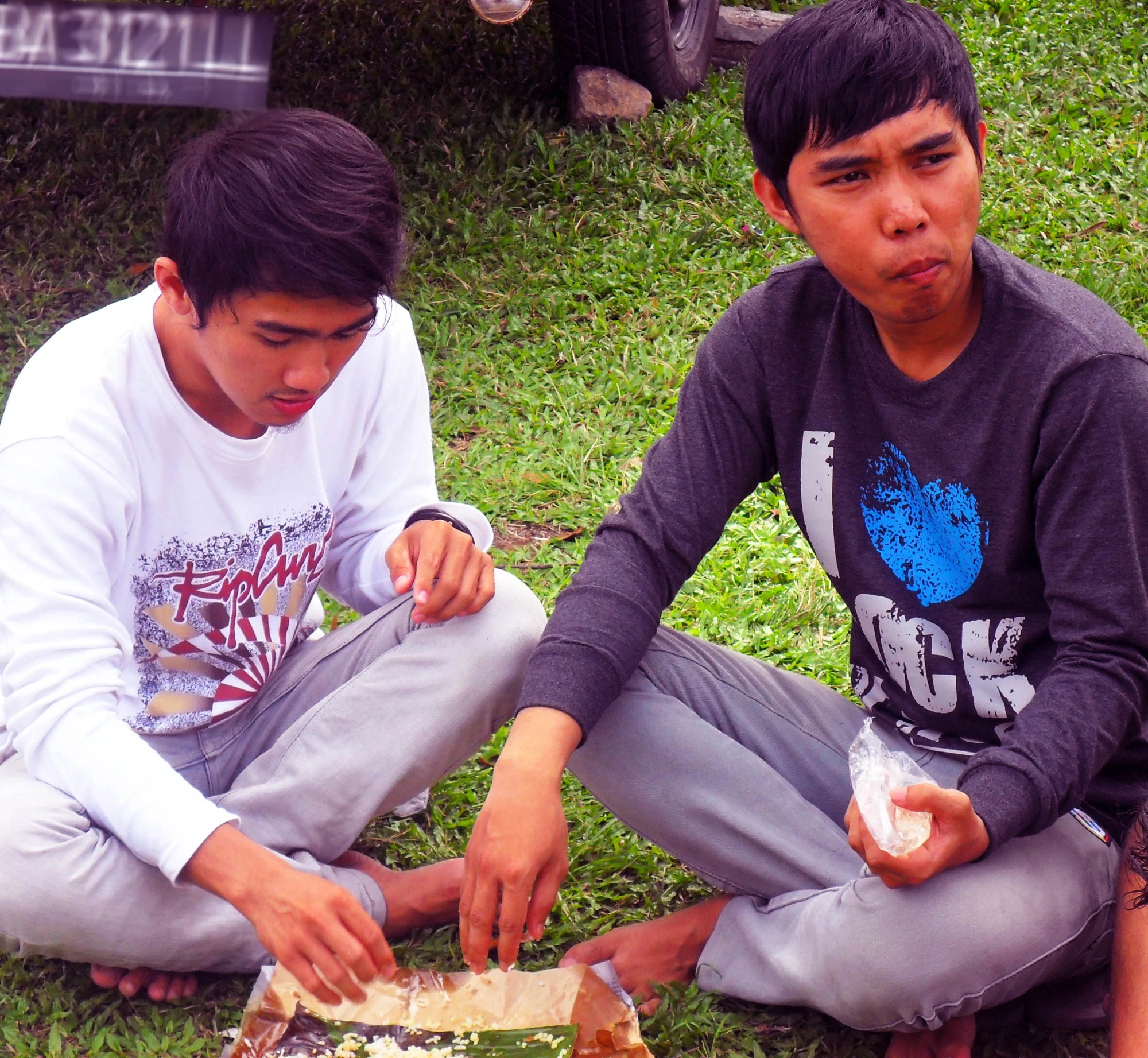 two young men sitting on the ground eating