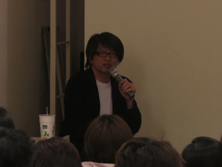 a young man speaking into a microphone in front of a group of people