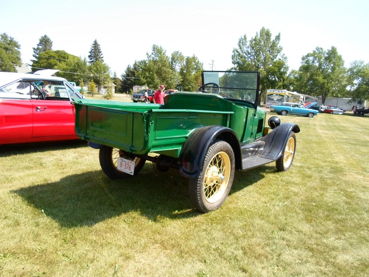 an old green truck parked next to other cars on grass