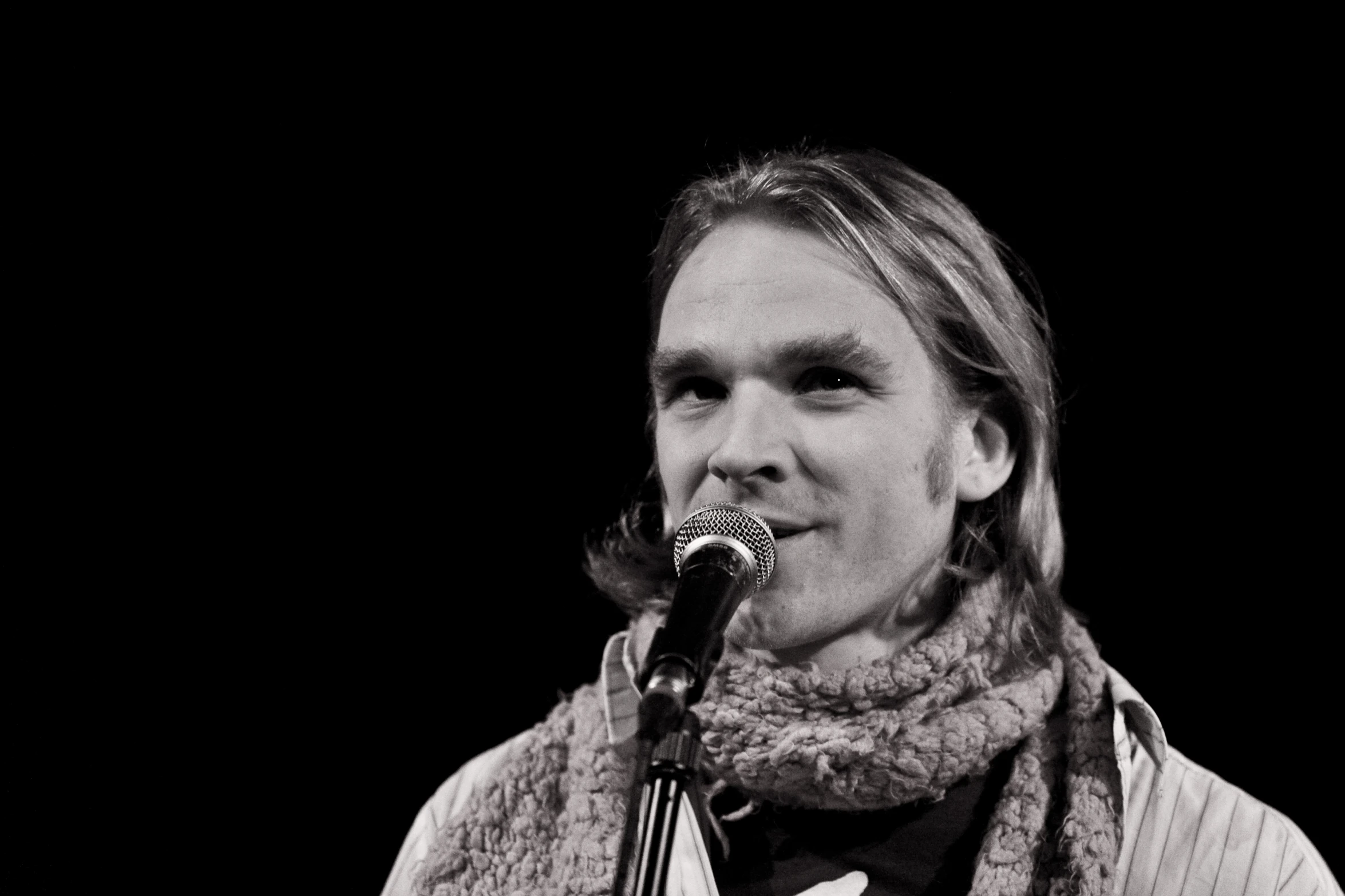 a man is singing into a microphone with a scarf around his neck