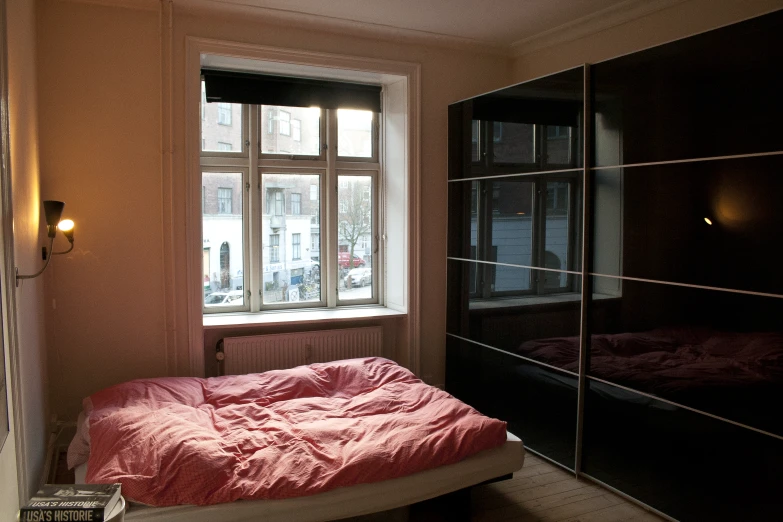 a bed sitting next to a window with a red comforter
