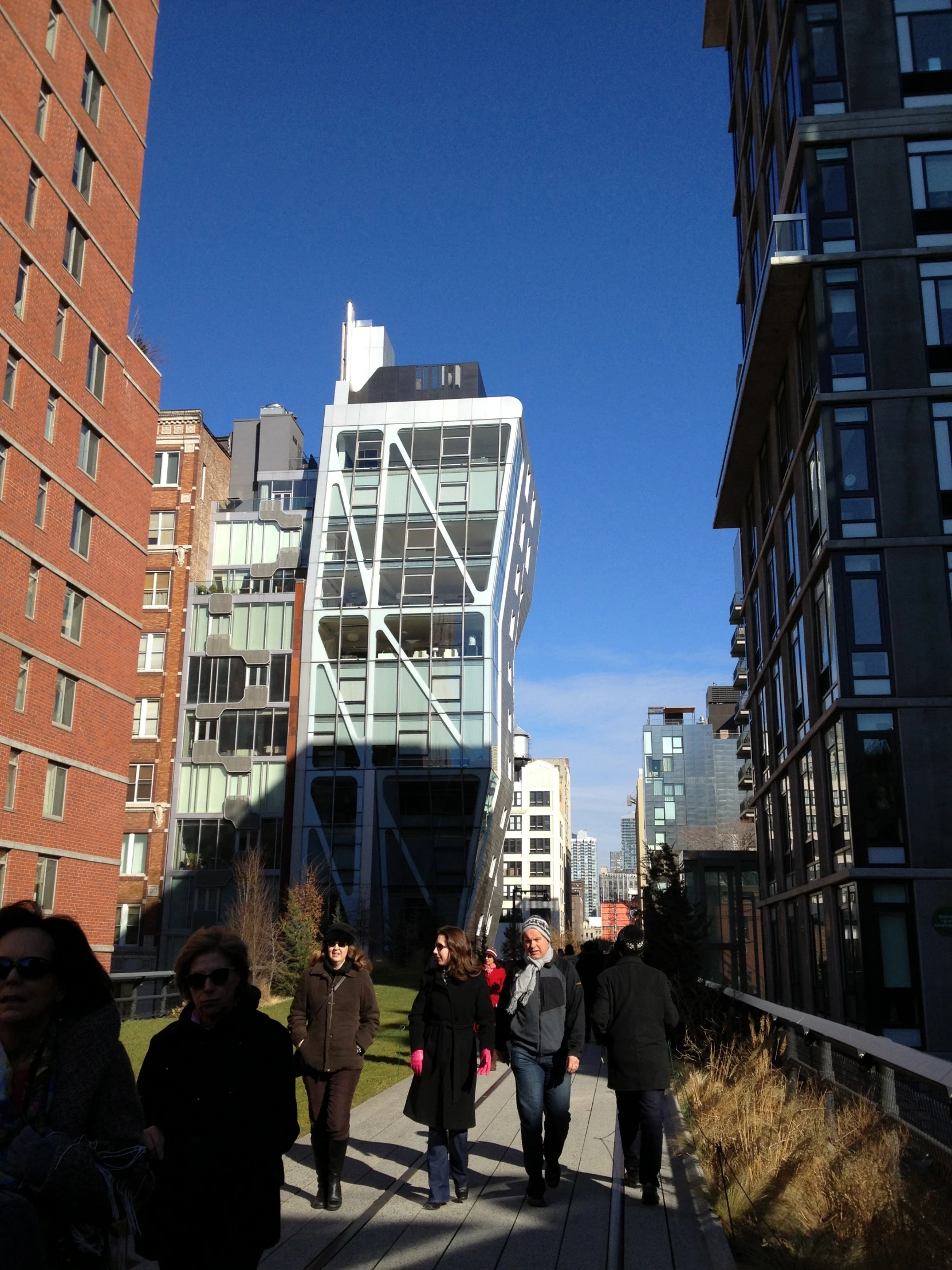 many people are walking down the sidewalk between buildings