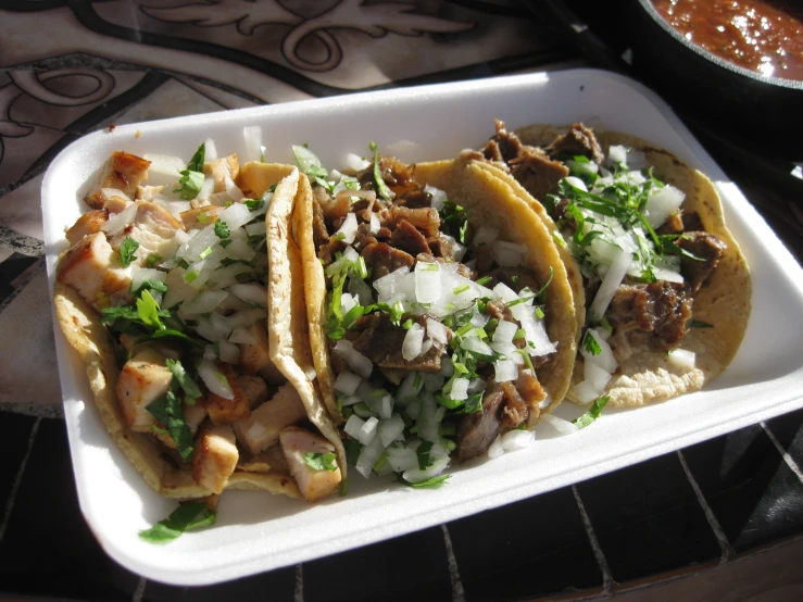 three tacos sit on a plate with onions and herbs