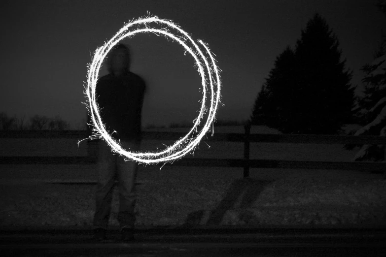 the man stands near the fence with his hand in his mouth as he holds a circular light art piece