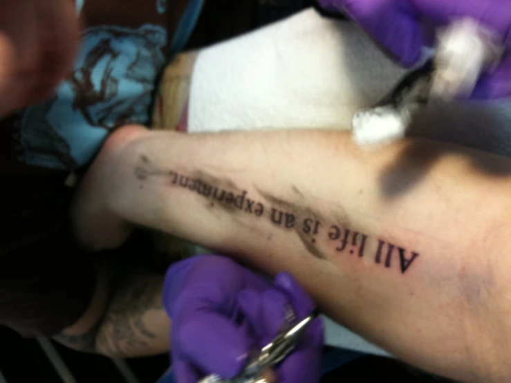 a man getting his arm tattooed with writing on it