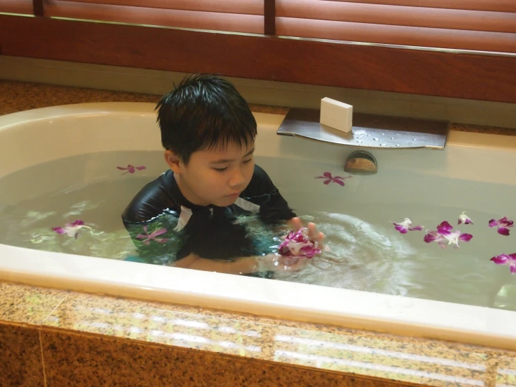 a boy in a tub of water playing with flowers