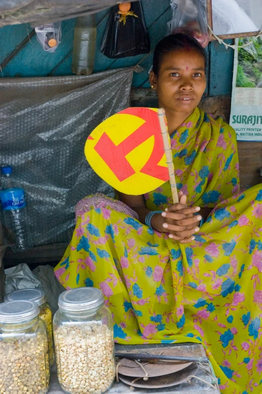 woman in colorful dress sitting at food vendor with jar of grains