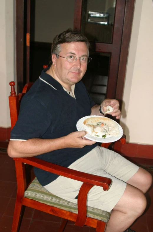 a man wearing a navy shirt sits while holding a plate with food on it