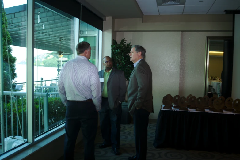 several men stand in front of large windows as they talk