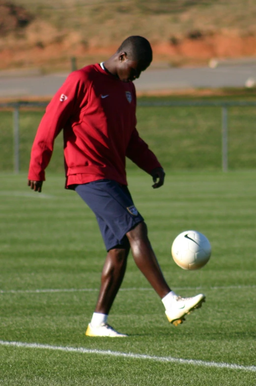 the soccer player wears a red shirt while kicking the ball