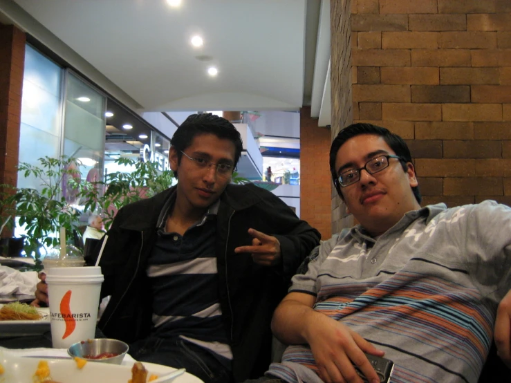 two young men sitting together and one pointing at soing