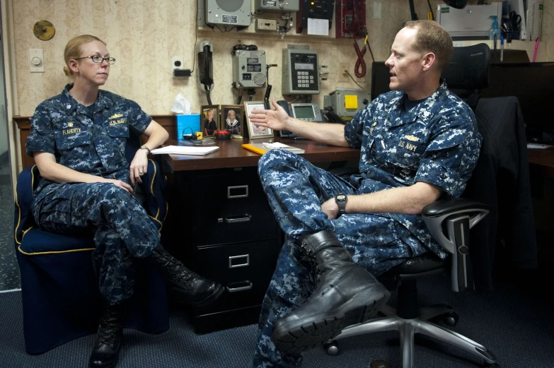 two men in uniforms sitting at a desk talking