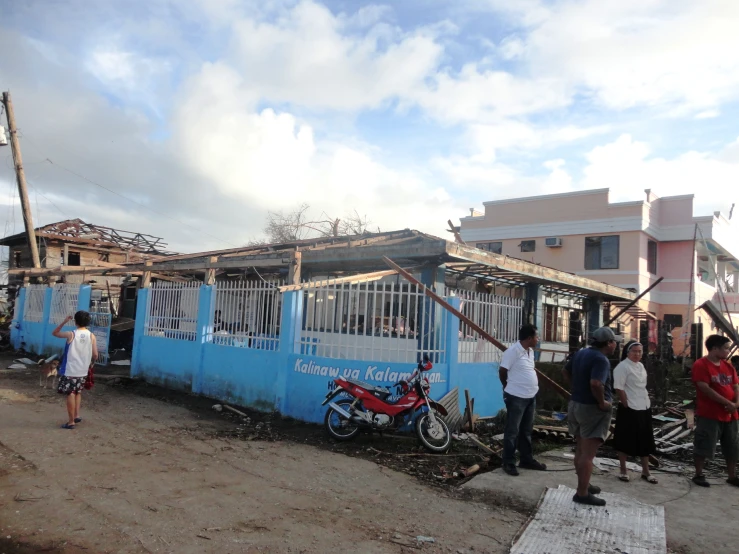 many people are gathered in the dirt outside a blue building