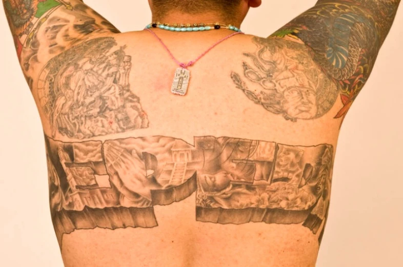a man with tattoos standing and holding his back to the camera