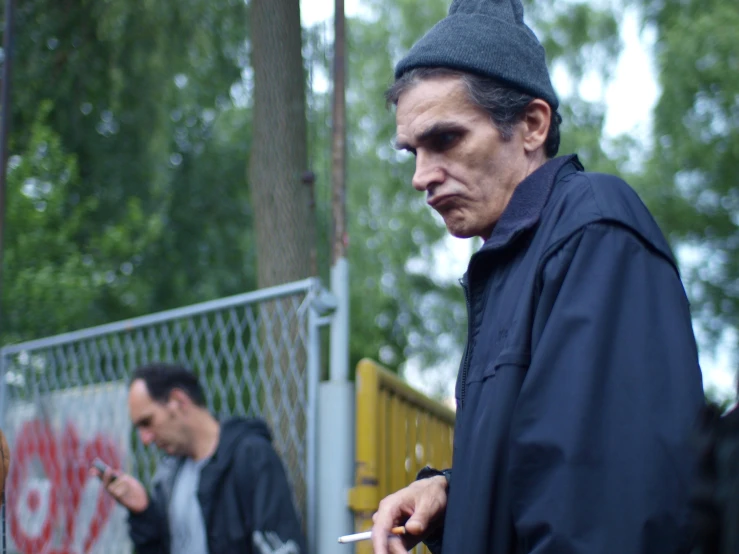 two people smoking while walking in front of a gate