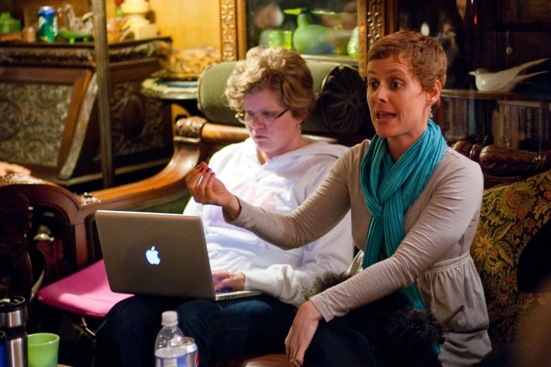 two women sit and look at a computer screen