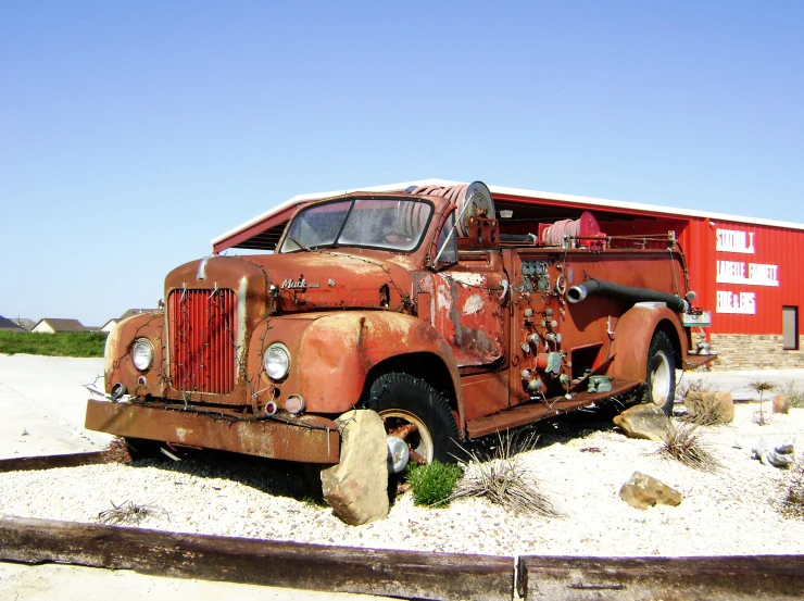 an old rusted truck parked on a patch of land next to a red building