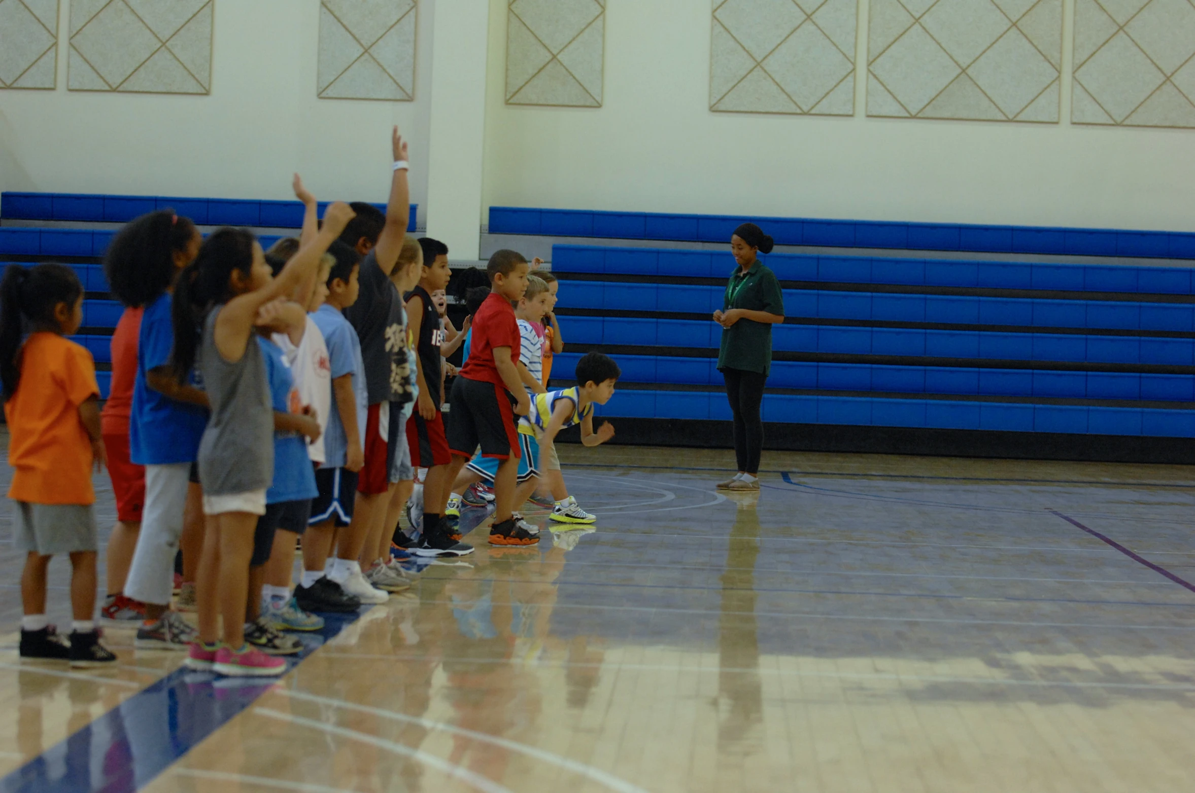 a group of children in basketball gear standing on a court while a woman stands in front of them