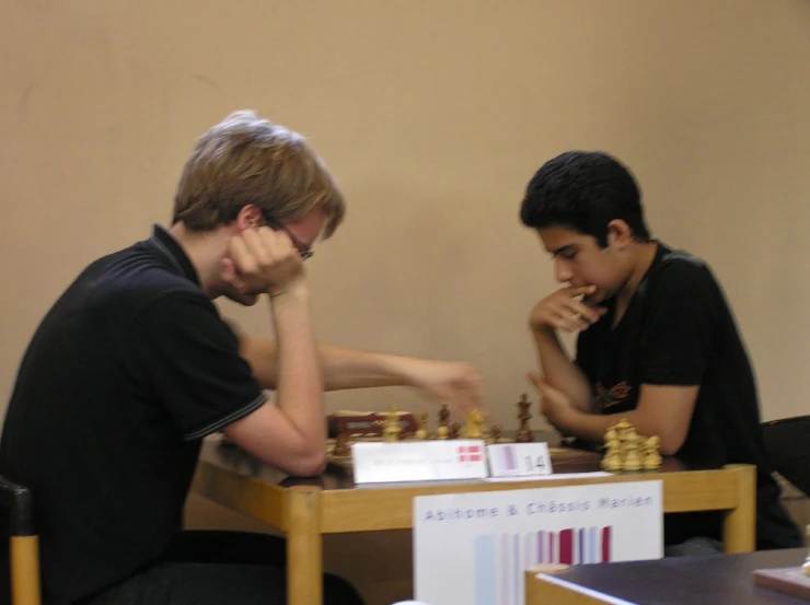 two men playing chess at a wooden table