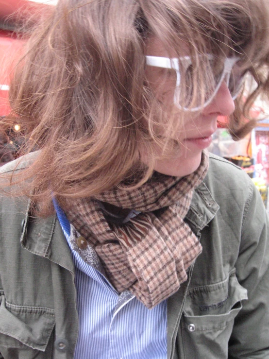 a woman with a jacket, tie and glasses staring down at her cell phone