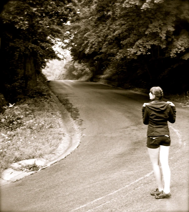 woman walking on paved roadway with trees behind