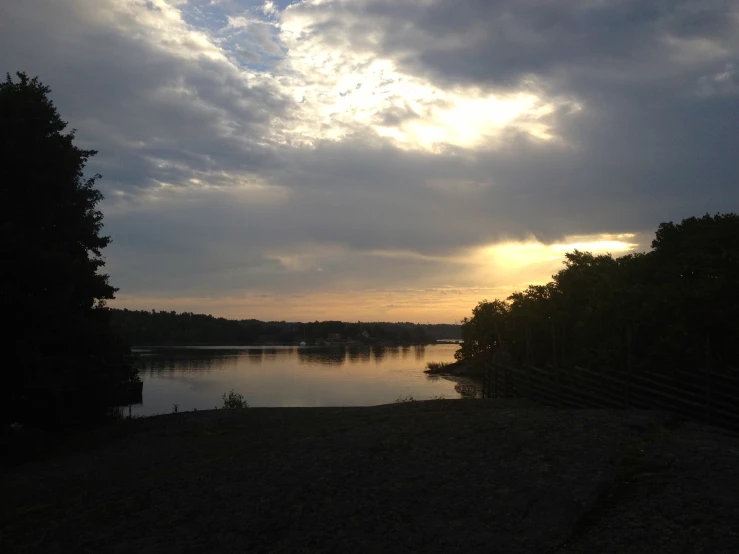 the sun is setting near the lake with cloudy skies