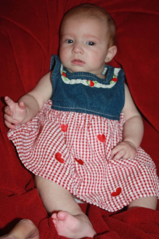 a baby girl sitting on a bed looking at the camera