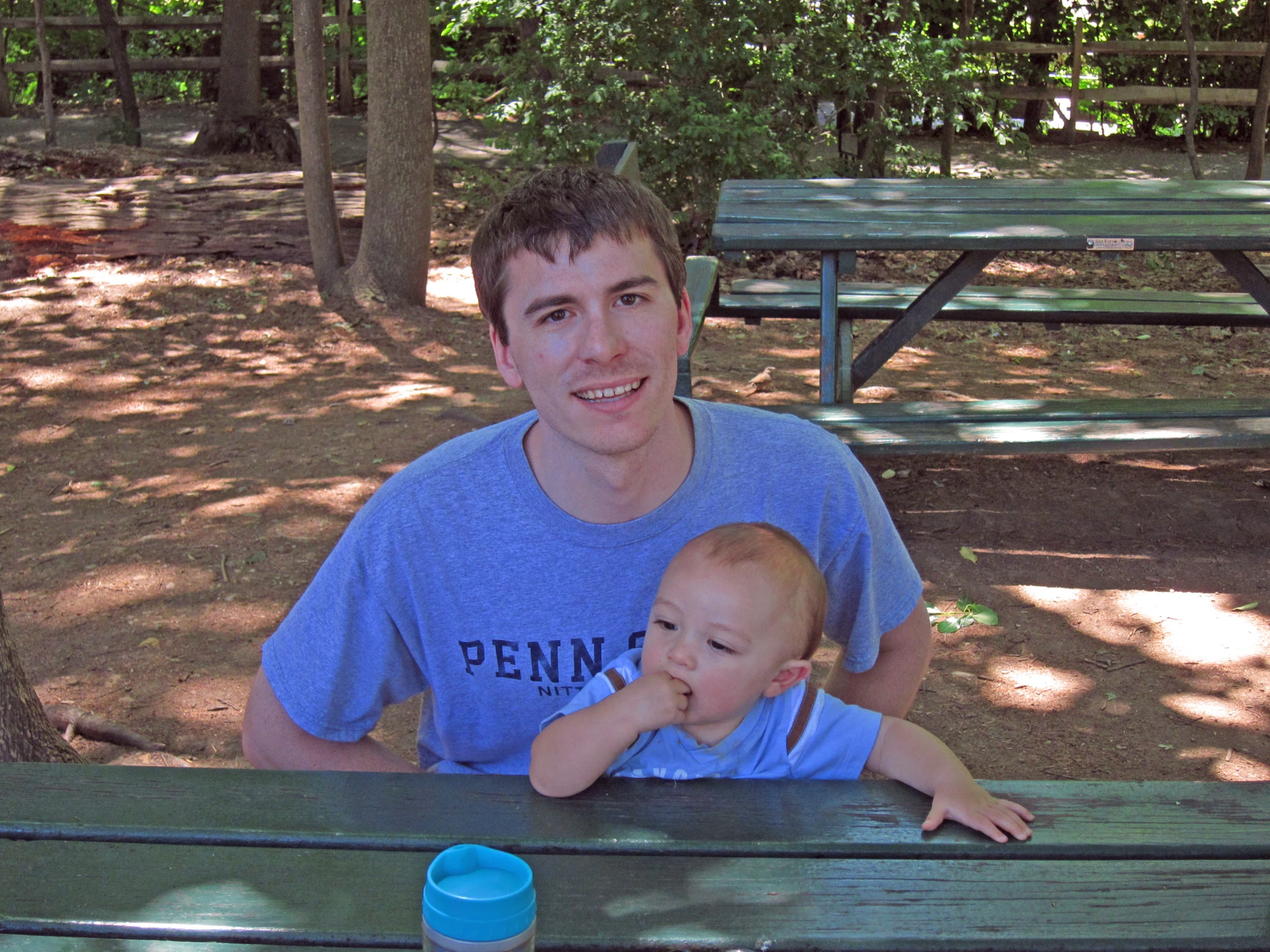 a young man holding a small baby next to picnic table