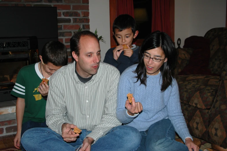 a man sitting on a couch eating food next to two children