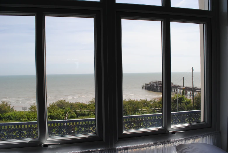 the view out a window shows a pier by the beach