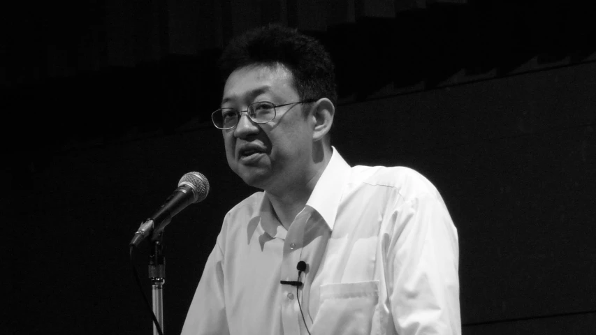 a man wearing glasses and a on up shirt holding a microphone