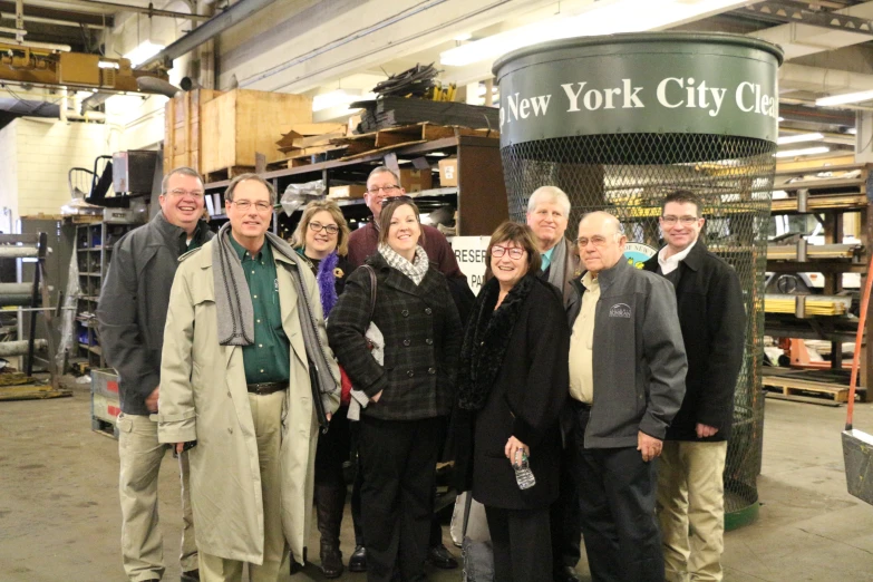 six people smiling at the camera next to a large sign