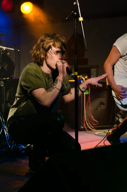 a young man sitting in front of a microphone while another man talks on the phone