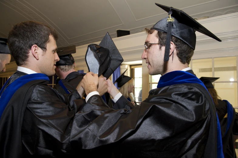 two men in graduation caps and gowns holding a large fan