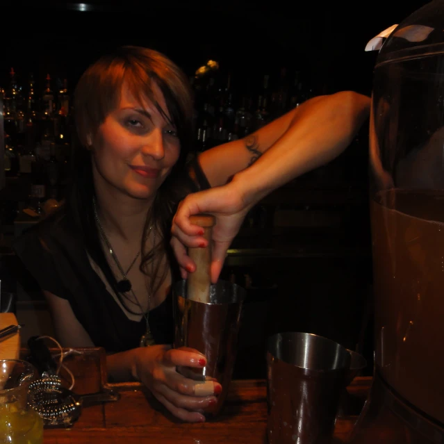 a woman sitting at a bar filling a drink with a blender