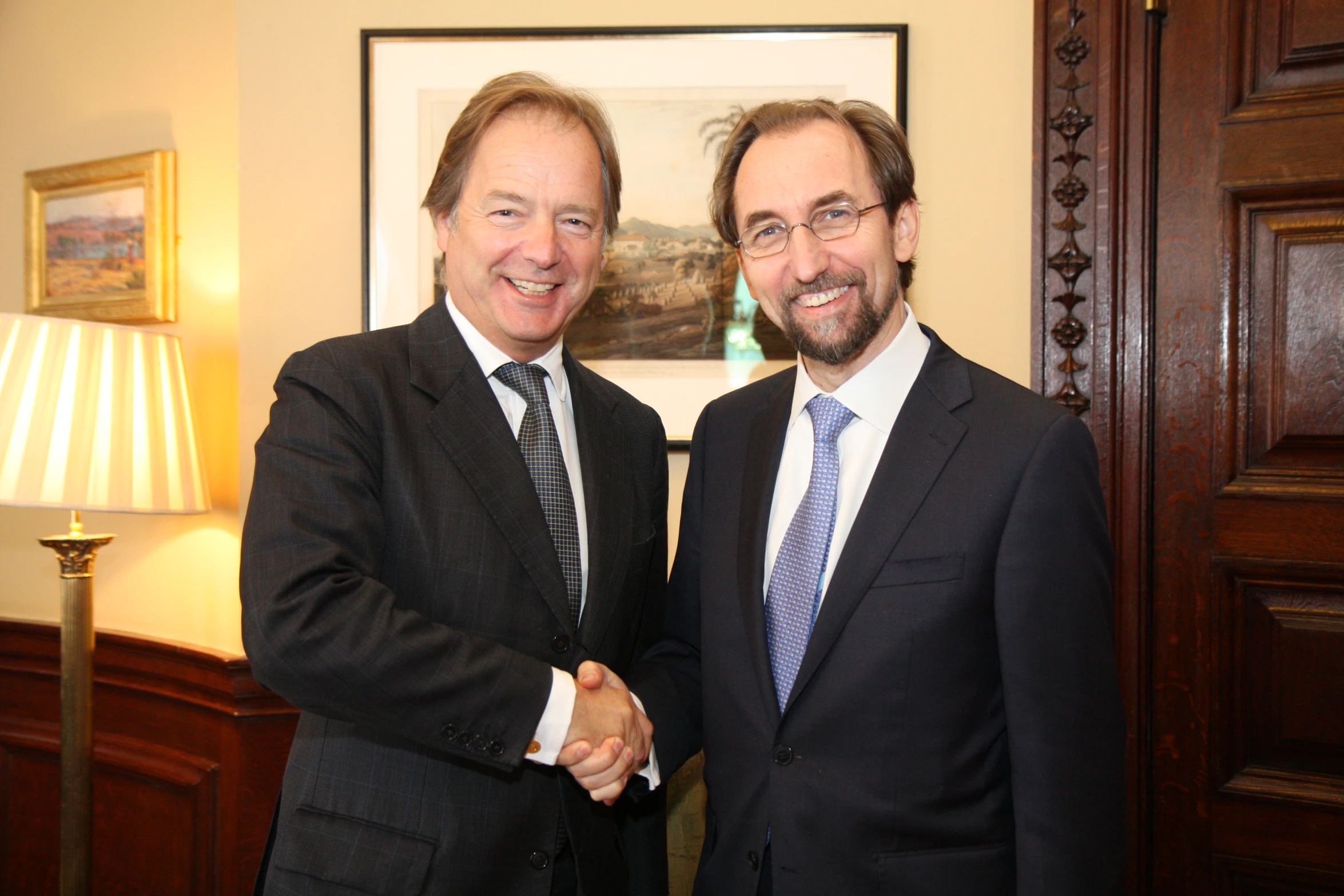 two businessmen smiling and shaking hands in front of paintings