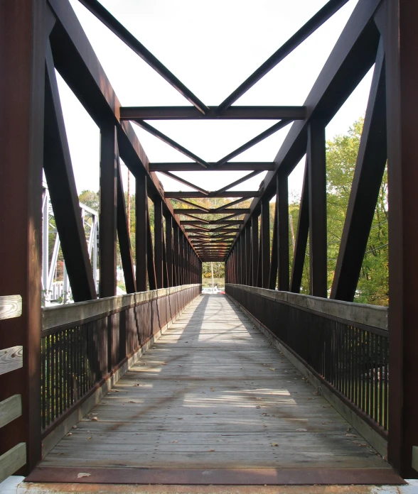 an empty wooden bridge with railings leads to another walkway