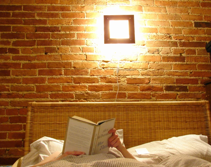 woman sitting in bed reading a book next to a lamp