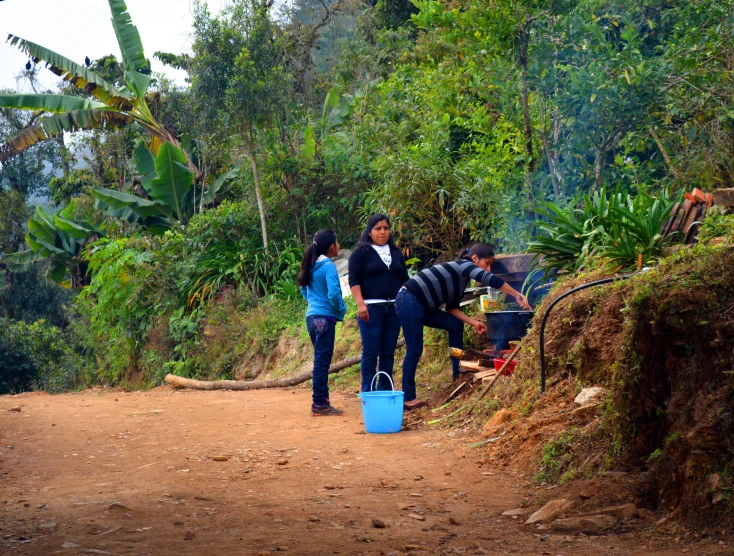 a group of people on a dirt road with two men carrying buckets of water