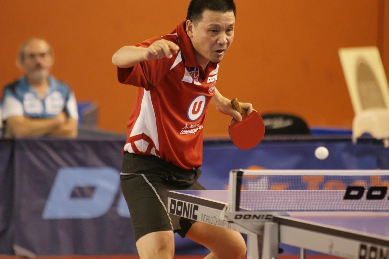 an asian man in red is holding a racket