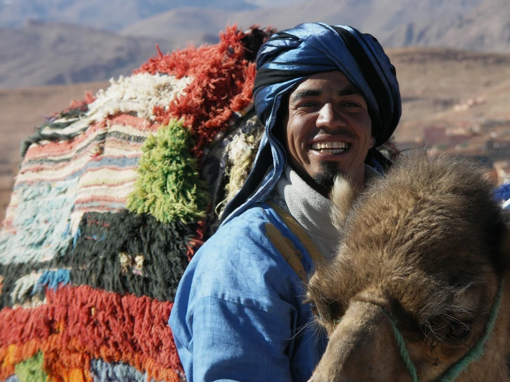 man in blue jacket and head scarf sitting on top of camel