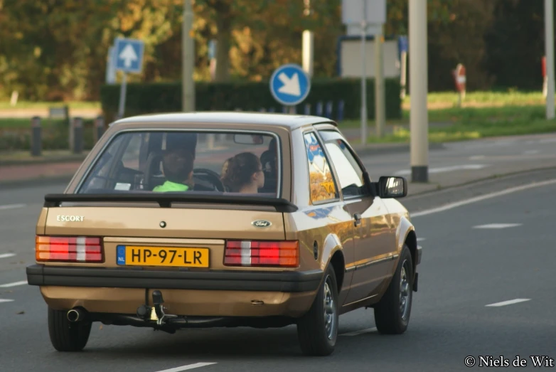 a brown car stopped at an intersection with trees in the background