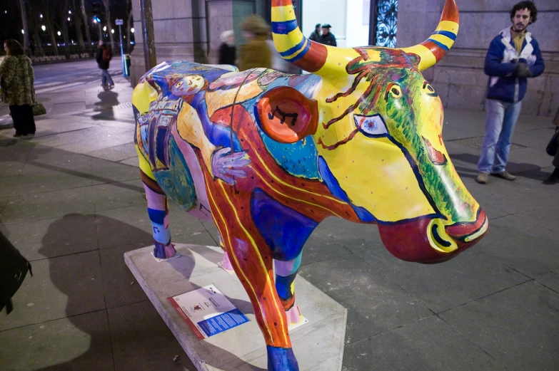 the big cow is colorful in color, and there are people around