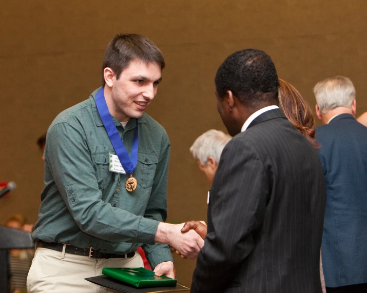 two men shaking hands at a meeting, one being honored